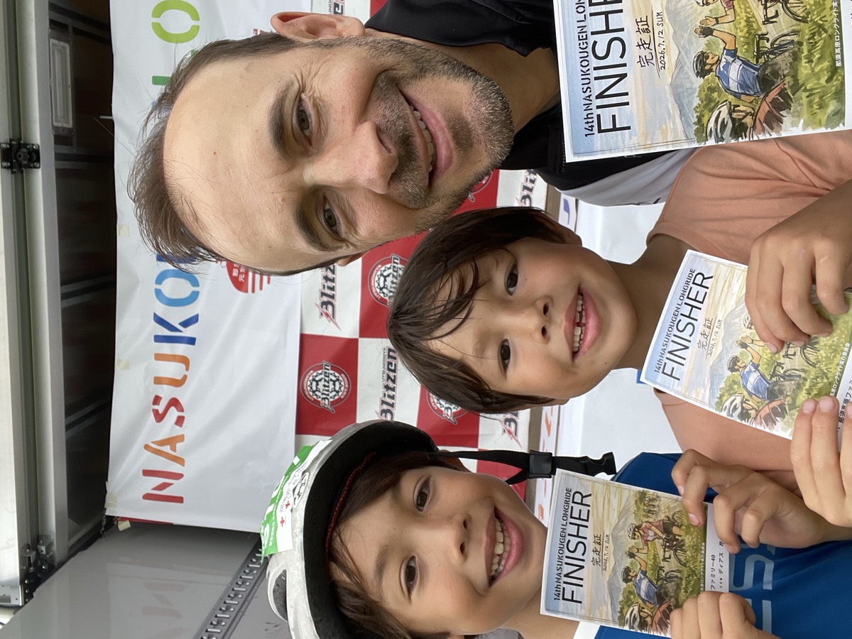 A selfie of a father and his two sons at the finish line, each holding a Nasukougen Longride finisher certificate.