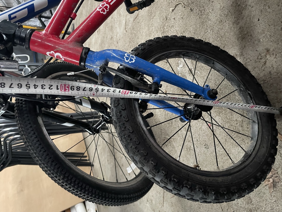 A tape measure held against the front wheel of a small child's bike, with a larger bike standing behind it.