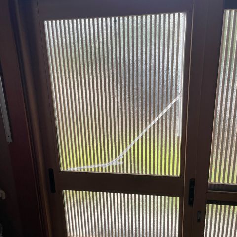 A ribbed frosted glass door panel with a long diagonal crack held together by white tape.