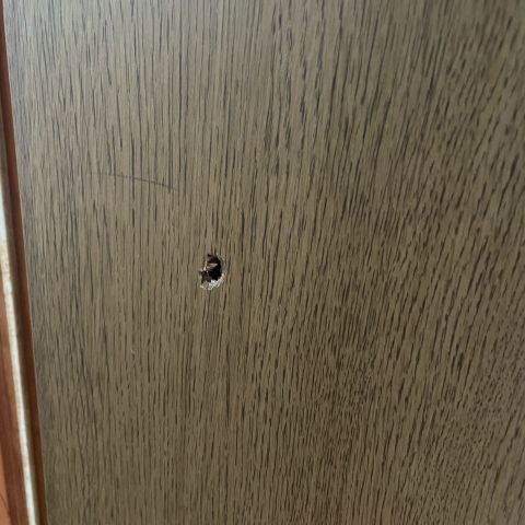 A small hole punched through a wood-grain door.