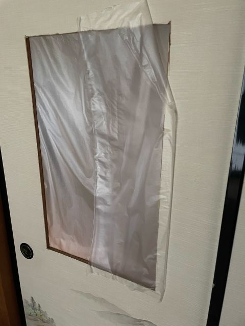 A paper sliding door with a large rectangular hole covered by clear plastic sheeting and tape.