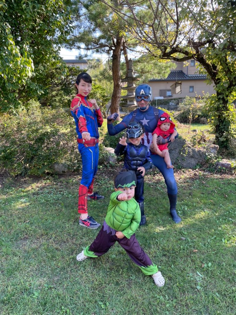 Our family in Marvel costumes in the garden: me as Captain America holding the baby dressed as Spider-Man, my wife as Captain Marvel, and the boys as Black Panther and the Hulk striking poses.