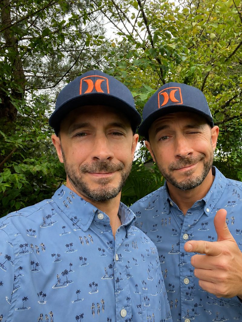 Two side-by-side images of Kevin Dias in the same blue Hawaiian shirt and navy Hurley cap, one smiling and one winking with a thumbs up.