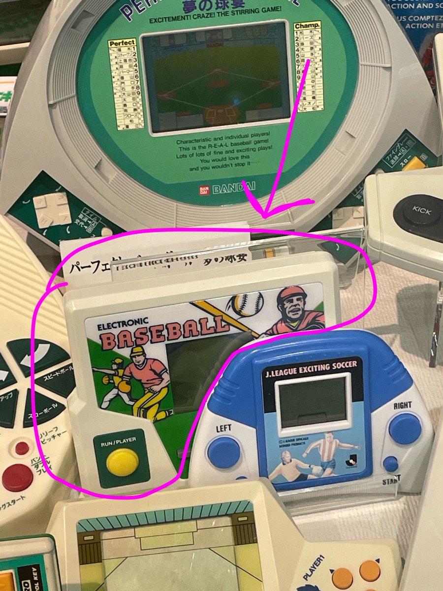A display case of vintage handheld electronic games at the Mibu Toy Museum, with a white Electronic Baseball handheld circled in pink.