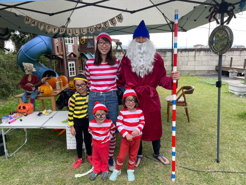 Our family under a Happy Halloween banner: me as Wizard Whitebeard in a red robe, white beard, and blue hat holding a striped staff, my wife and two kids as Waldo, and our oldest as Odlaw.