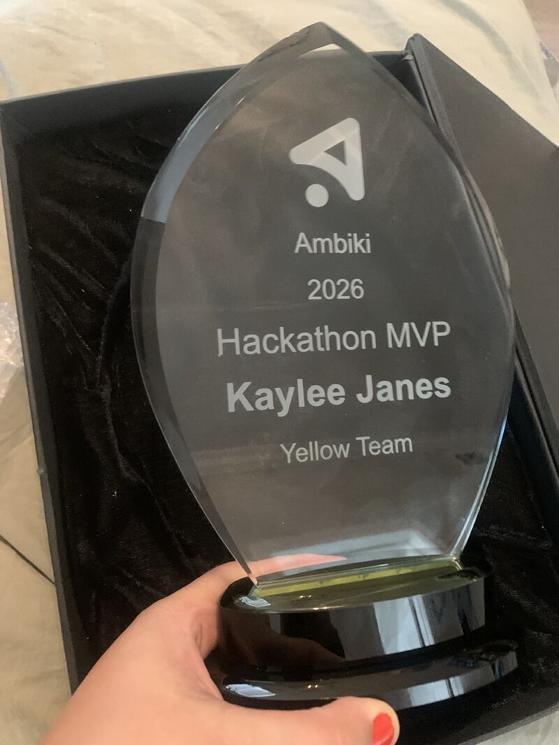 A crystal trophy engraved with the Ambiki logo, Ambiki 2026 Hackathon MVP, Kaylee Janes, Yellow Team, held above its black presentation box.