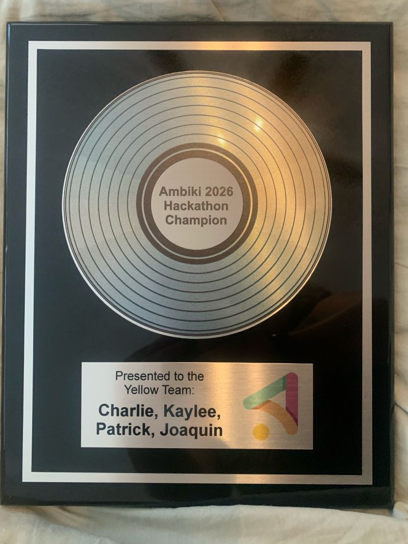 A black plaque with a silver record reading Ambiki 2026 Hackathon Champion, presented to the Yellow Team: Charlie, Kaylee, Patrick, Joaquin.